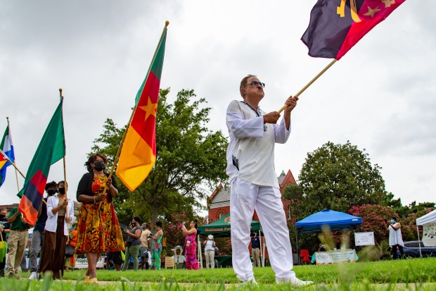 Calvin Pearson, in white, founder of Project 1619, walks with a flag at the opening of the 1619 Commemoration at Fort Monroe on Saturday, August 21, 2021 in Hampton, Va. (Mike Caudill / For The Virginian-Pilot)